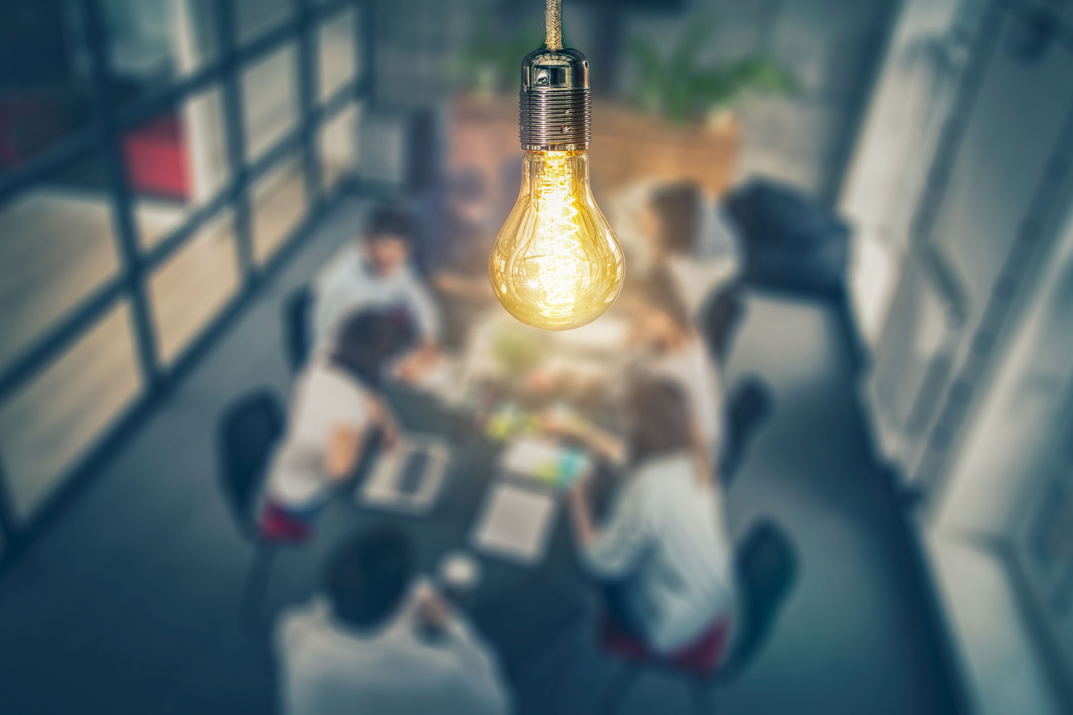 image of a lit bulb on top of a table at which entpreneurs are seated at